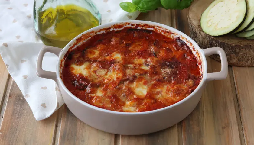 Parmigiana di melanzane appena sfornata, dorata e filante, con pomodoro e basilico fresco.
