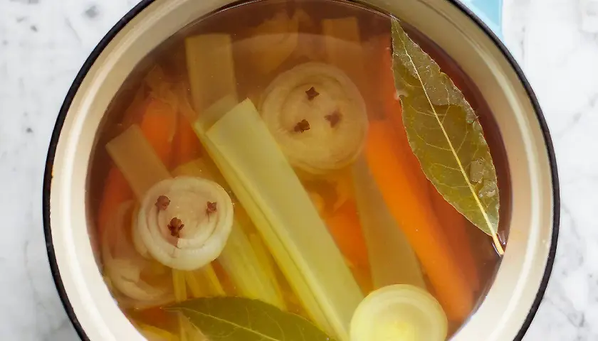 Brodo vegetale ricetta: carote, sedano, cipolla con chiodi di garofano e alloro in pentola.