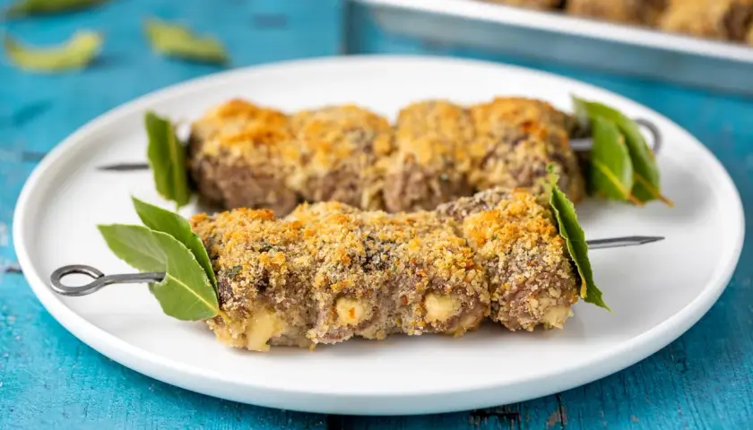 Braciole alla messinese su spiedini, impanate e dorate, guarnite con foglie di alloro.