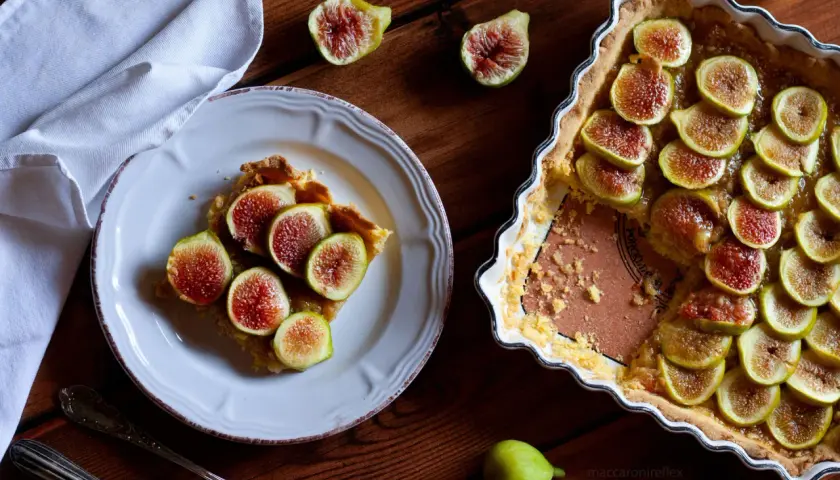 Deliziosi dolci con fichi freschi, una fetta su un piatto bianco e la torta intera in una teglia.