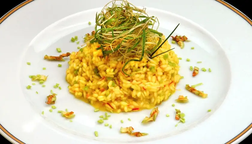 Risotto giallo intenso con fiori di zucca e zafferano, guarnito con erbe croccanti.