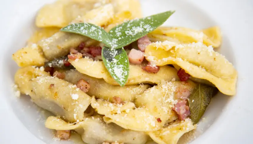 Un piatto di casoncelli alla bergamasca, conditi con burro, salvia e pancetta croccante, spolverati di parmigiano.