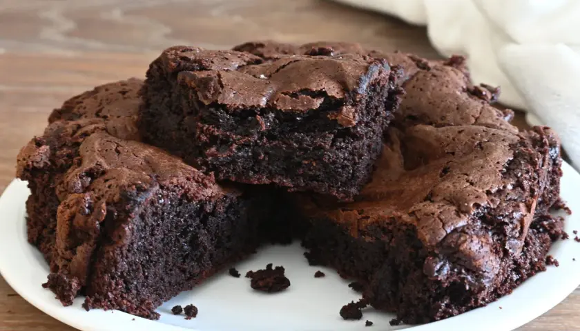 Torta al cioccolato, soffice e umida, tagliata a fette su un piatto bianco. La crosta è leggermente screpolata, rivelando l'interno scuro e invitante.