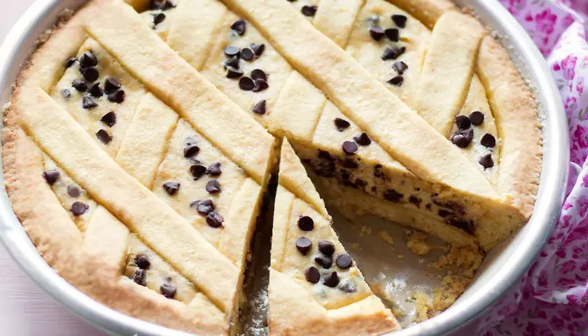 Una deliziosa crostata di ricotta con gocce di cioccolato, con una fetta tagliata per mostrare il ripieno cremoso.