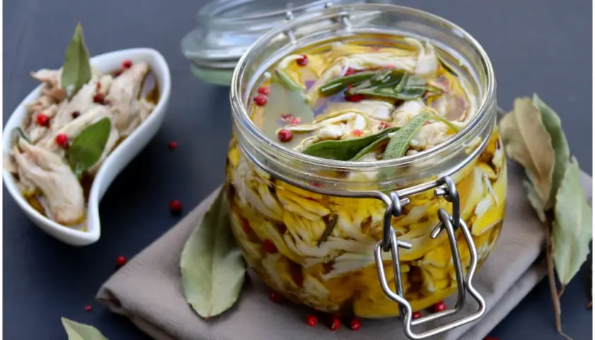 Tonno di coniglio sott'olio, sfilacciato e conservato in un barattolo di vetro con erbe aromatiche e pepe rosa.