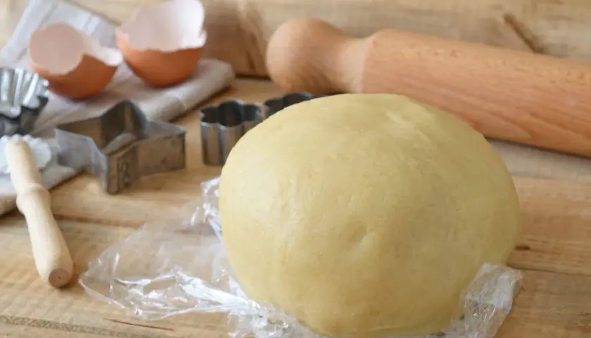 Impasto per crostata pronto, con stampini, uovo rotto e mattarello. La pasta frolla friabile per crostata è perfetta per dolci fatti in casa.