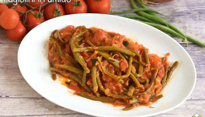 Fagiolini in umido, un piatto saporito con fagiolini verdi cotti in un sugo di pomodoro e cipolla, accompagnato da pomodorini freschi.