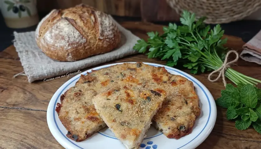 Frittata di pane dorata e saporita, servita su un piatto bianco con bordi blu, accanto a pane fresco e erbe aromatiche.