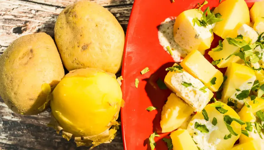 Patate fresche e un'appetitosa insalata di patate condita con erbe aromatiche su un piatto rosso.