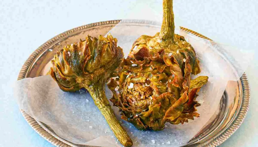 Due carciofi alla giudia dorati e croccanti, cosparsi di sale grosso, su un vassoio d'argento.