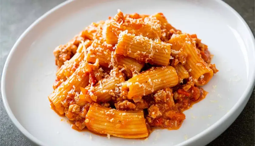 Un piatto di pasta alla zozzona, con rigatoni conditi con un ricco ragù di carne e abbondante parmigiano grattugiato.