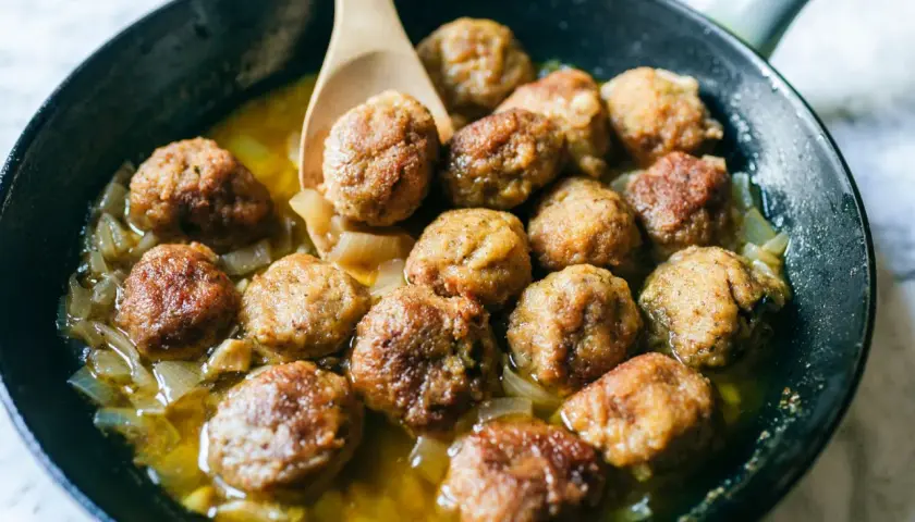 Polpette in bianco succulente in padella con cipolle caramellate, pronte per essere gustate.