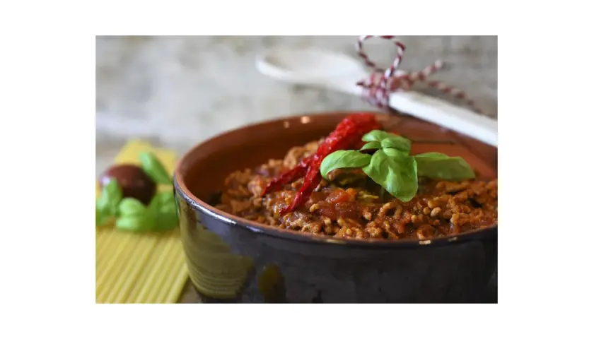 Un saporito ragù di verdure, guarnito con peperoncino e basilico, in una ciotola di terracotta.