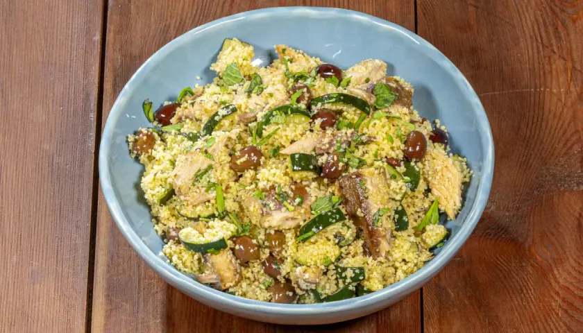 Un saporito cous cous con verdure, olive e pesce, guarnito con erbe fresche.