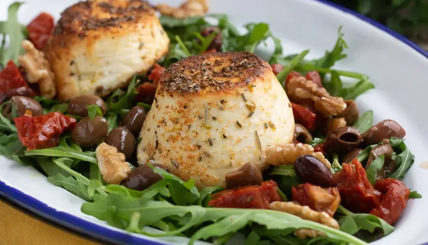 Due dischi di ricotta al forno su un letto di rucola, pomodori secchi, olive e noci.