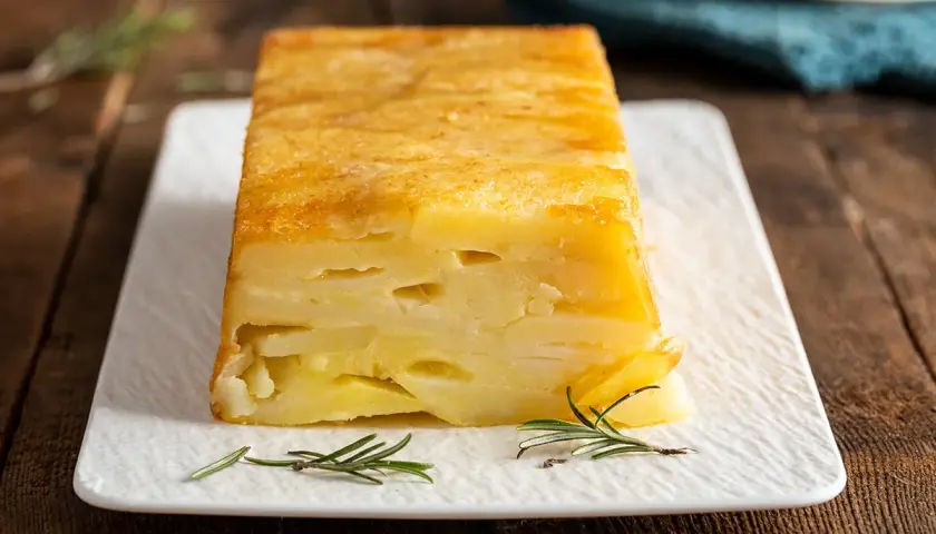 Sformato di patate a fette dorato e invitante, servito su un piatto bianco con rametti di rosmarino.