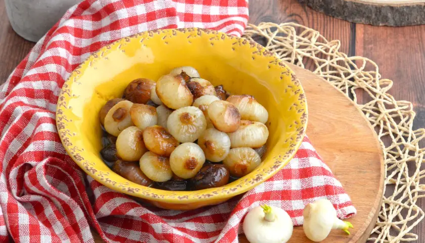 Cipolline in agrodolce caramellate in una ciotola gialla, servite su un tagliere di legno con tovagliolo a quadri rossi.