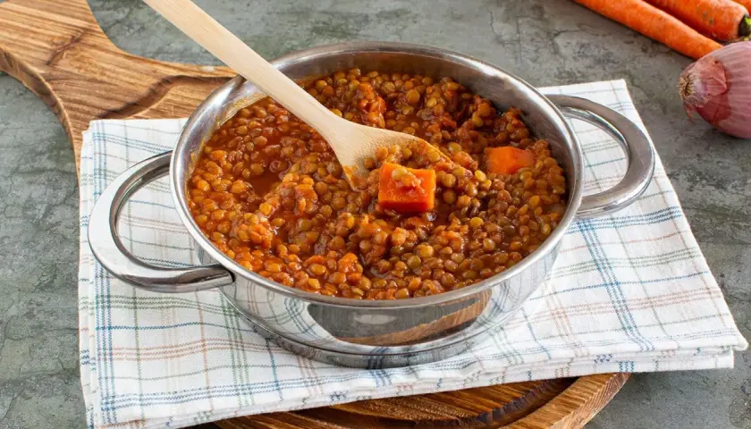 Un pentolino pieno di saporito ragù di lenticchie, con pezzi di carota e un cucchiaio di legno.