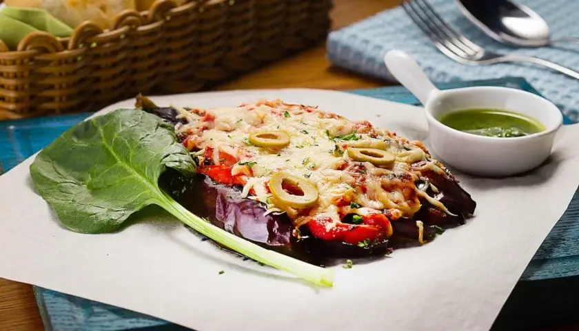 Caponata di melanzane gratinata con olive, pomodoro e formaggio fuso, servita con spinaci freschi e salsa verde.
