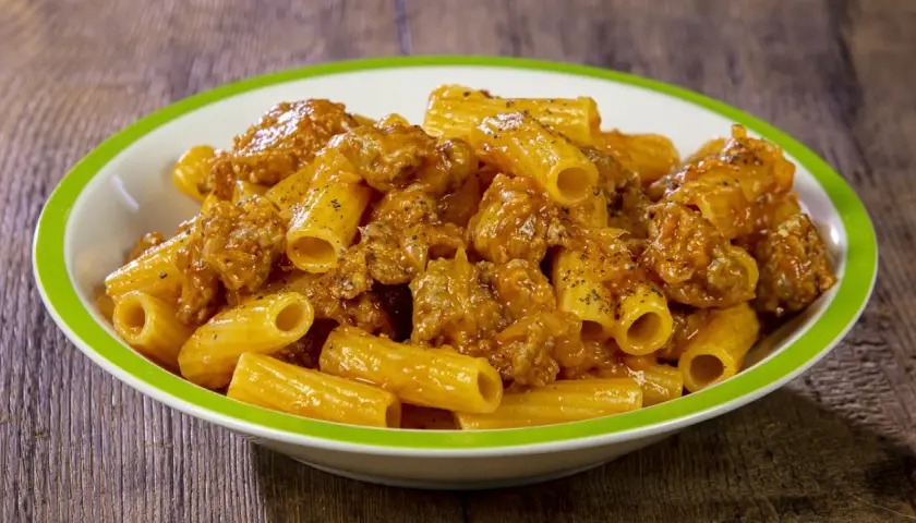 Piatto di rigatoni conditi con un ricco sugo di salsiccia, cosparso di pepe nero.