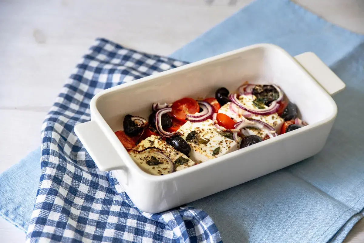 Feta al forno con pomodorini, olive nere e cipolla rossa, condita con erbe aromatiche.
