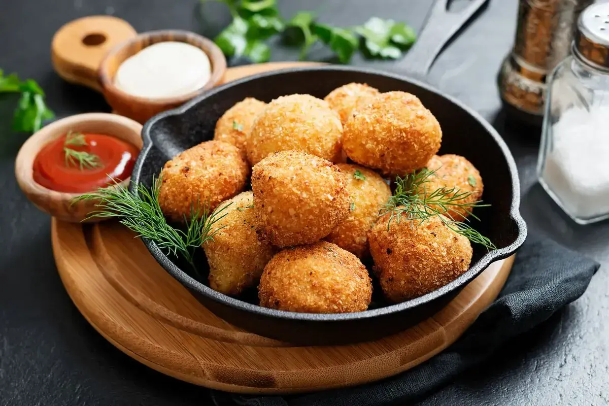 Croccanti polpette di zucca dorate servite in una padella di ghisa, con salse e erbe aromatiche.