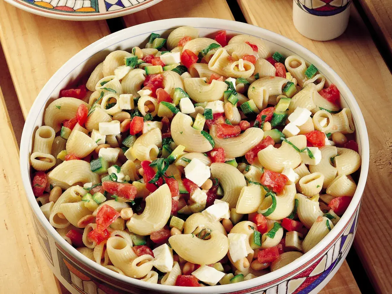 Un invitante piatto di pasta fredda con zucchine, pomodorini, cubetti di formaggio e fagioli, perfetto per un pasto estivo.