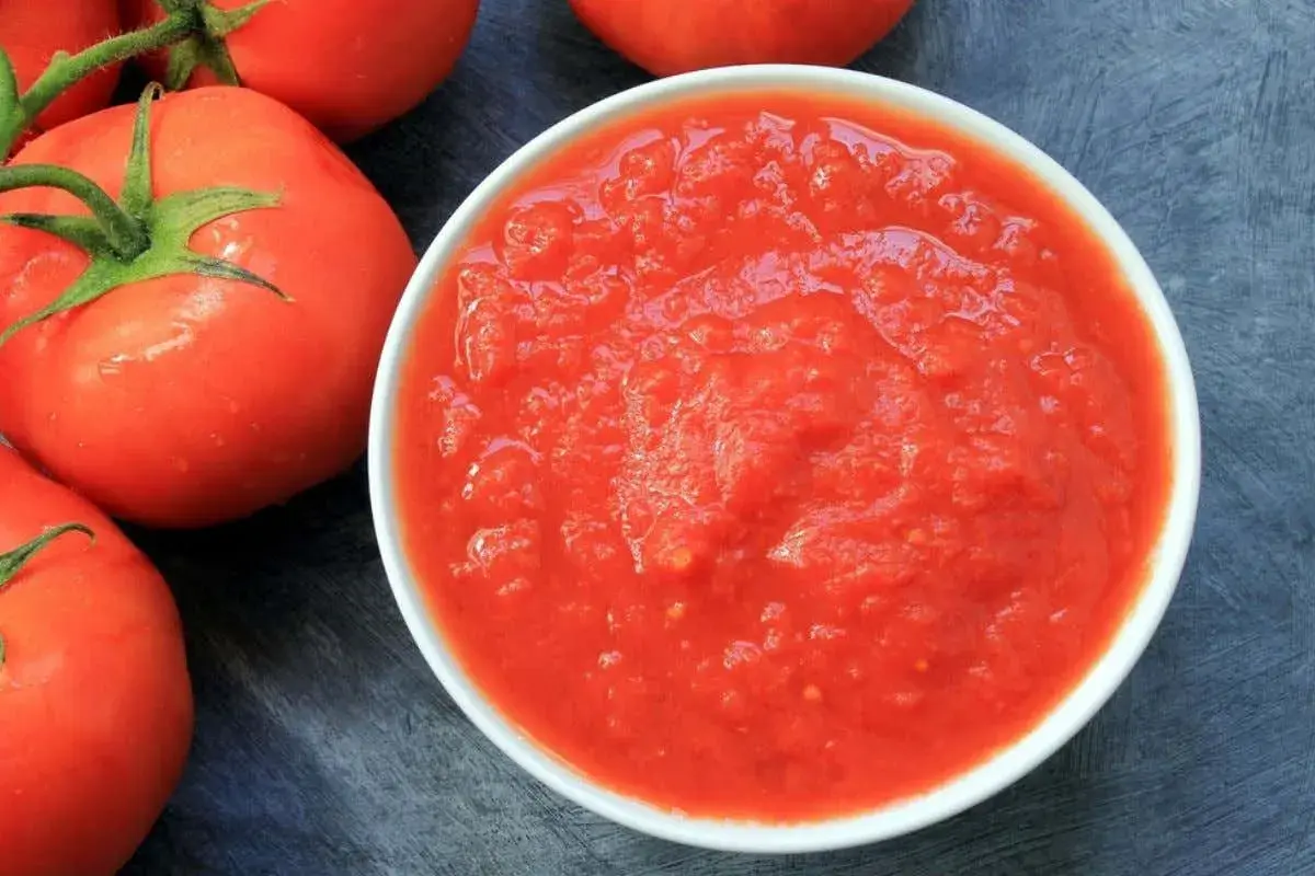Una ciotola di passata di pomodoro, con pomodori freschi sullo sfondo.