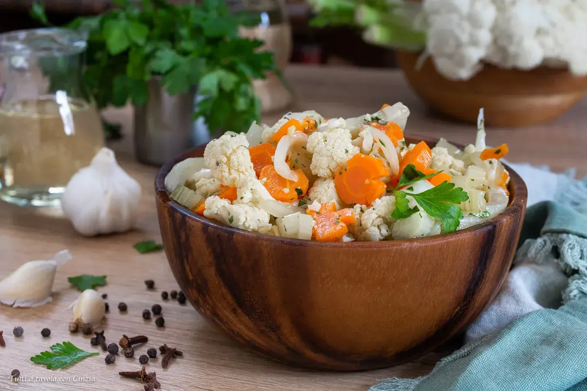 Una ciotola di legno piena di giardiniera fatta in casa, con cavolfiore, carote e cipolle, guarnita con prezzemolo fresco.