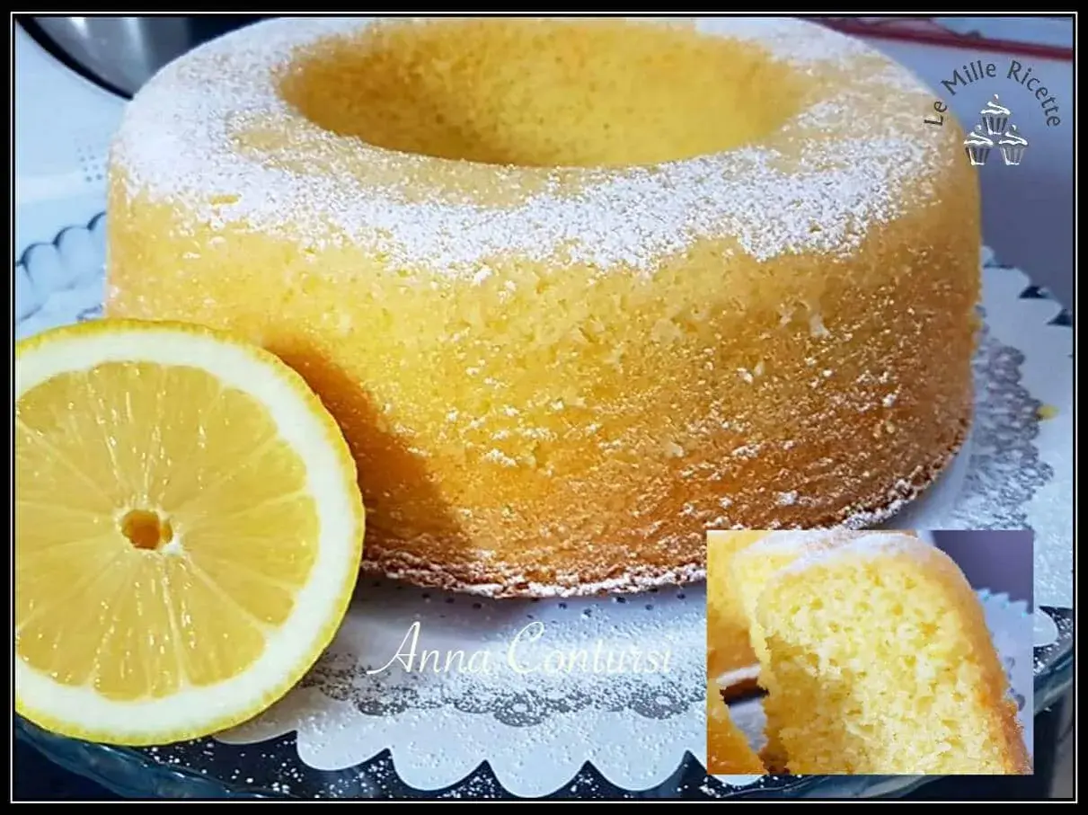 Un soffice ciambellone al limone, spolverato di zucchero a velo, accanto a una fetta di limone fresca.