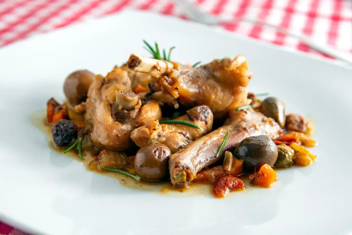 Coniglio alla cacciatora ricetta della nonna: succulenti pezzi di coniglio con olive, pomodorini e rosmarino, un classico sapore di casa.