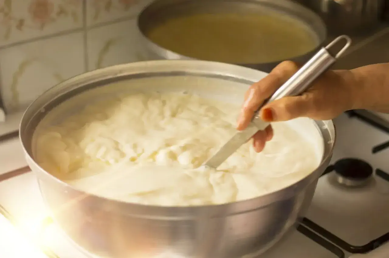 Mano che mescola un pentolone pieno di cremoso yogurt fatto in casa, pronto per essere gustato.