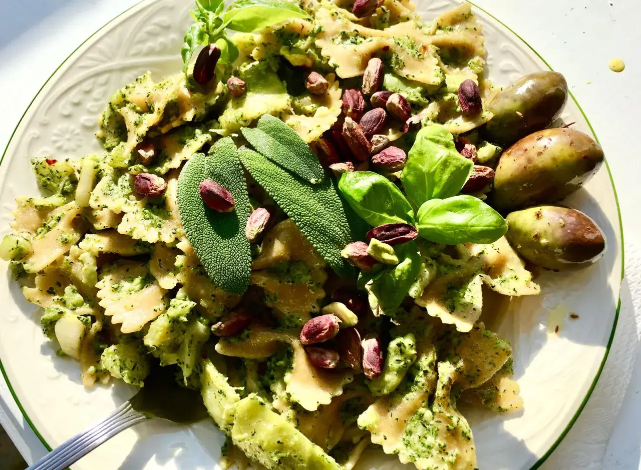 Farfalle condite con un cremoso pesto di salvia, guarnite con pistacchi, basilico e olive verdi.