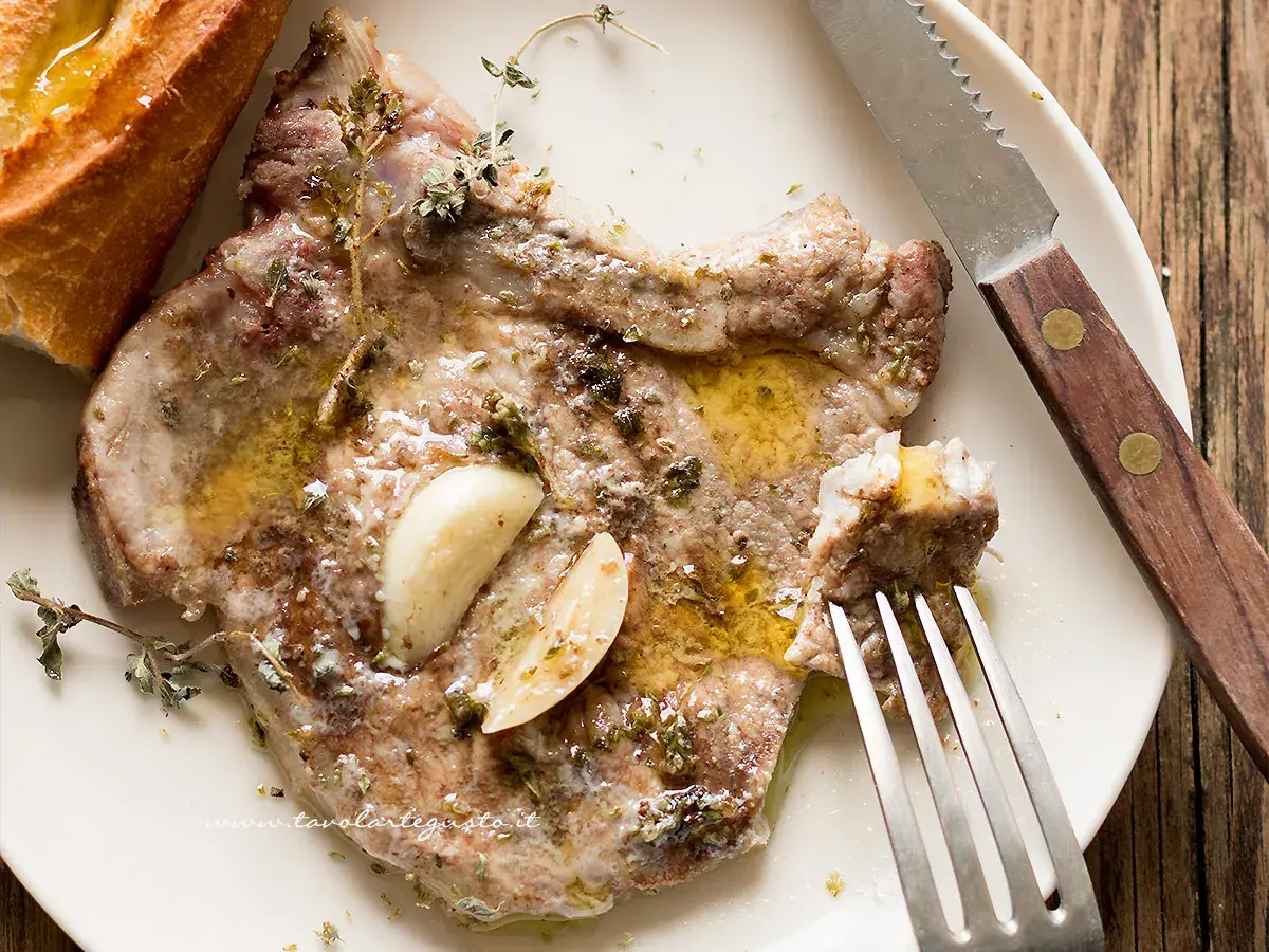 Succulente braciole di maiale cotte con aglio e erbe aromatiche, servite con pane croccante e un filo d'olio.