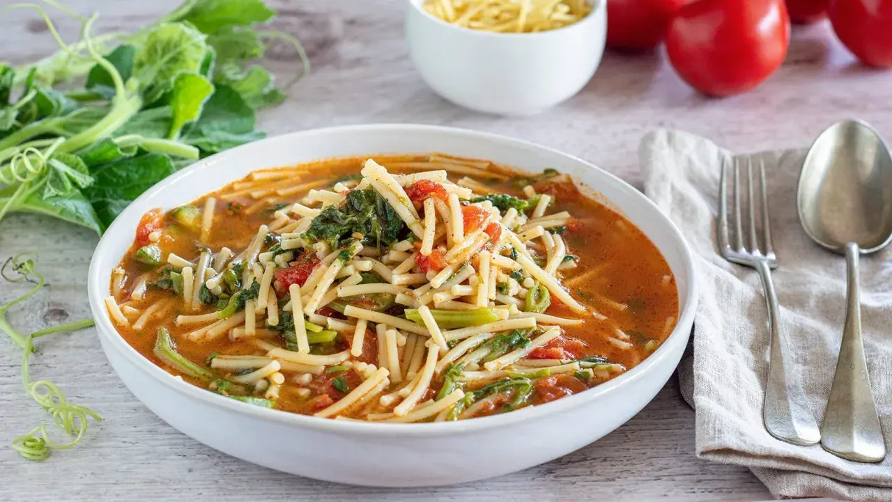 Un piatto fumante di pasta con i tenerumi, un classico siciliano, con pomodoro e verdure fresche.