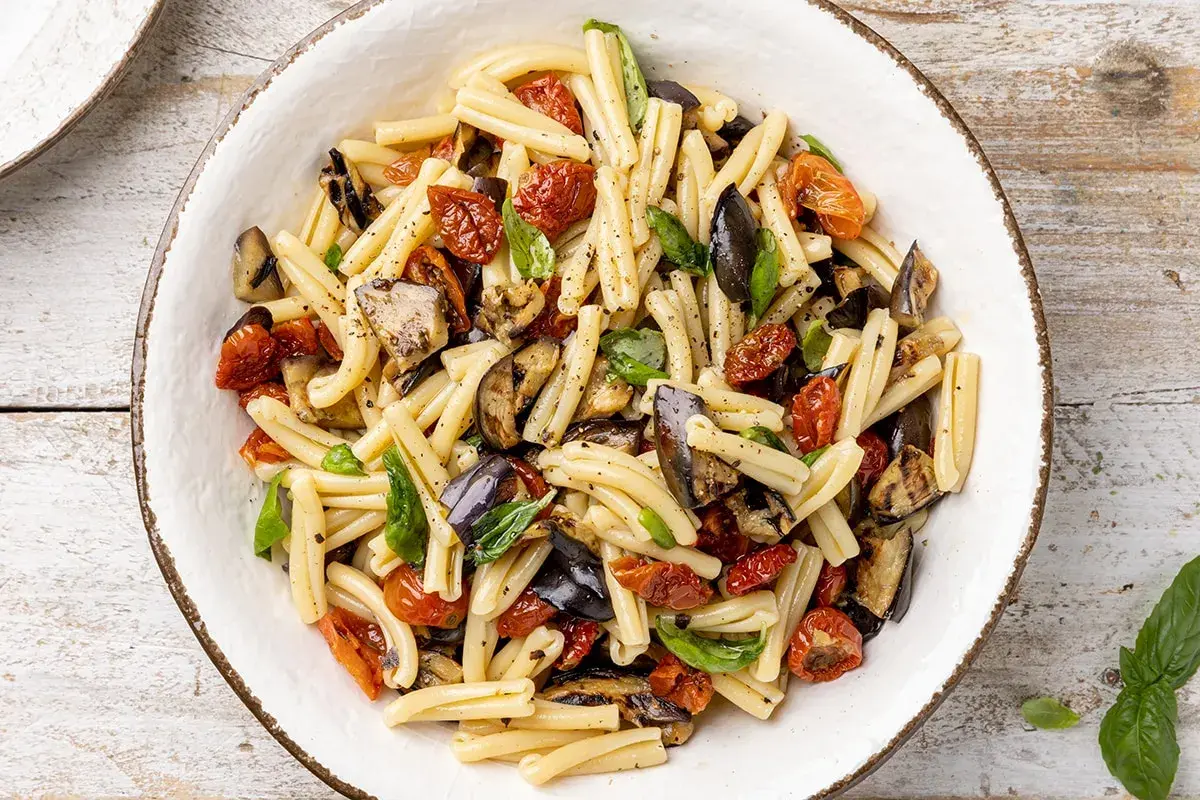 Pasta fredda con melanzane grigliate, pomodorini secchi e basilico fresco, un piatto estivo colorato e saporito.