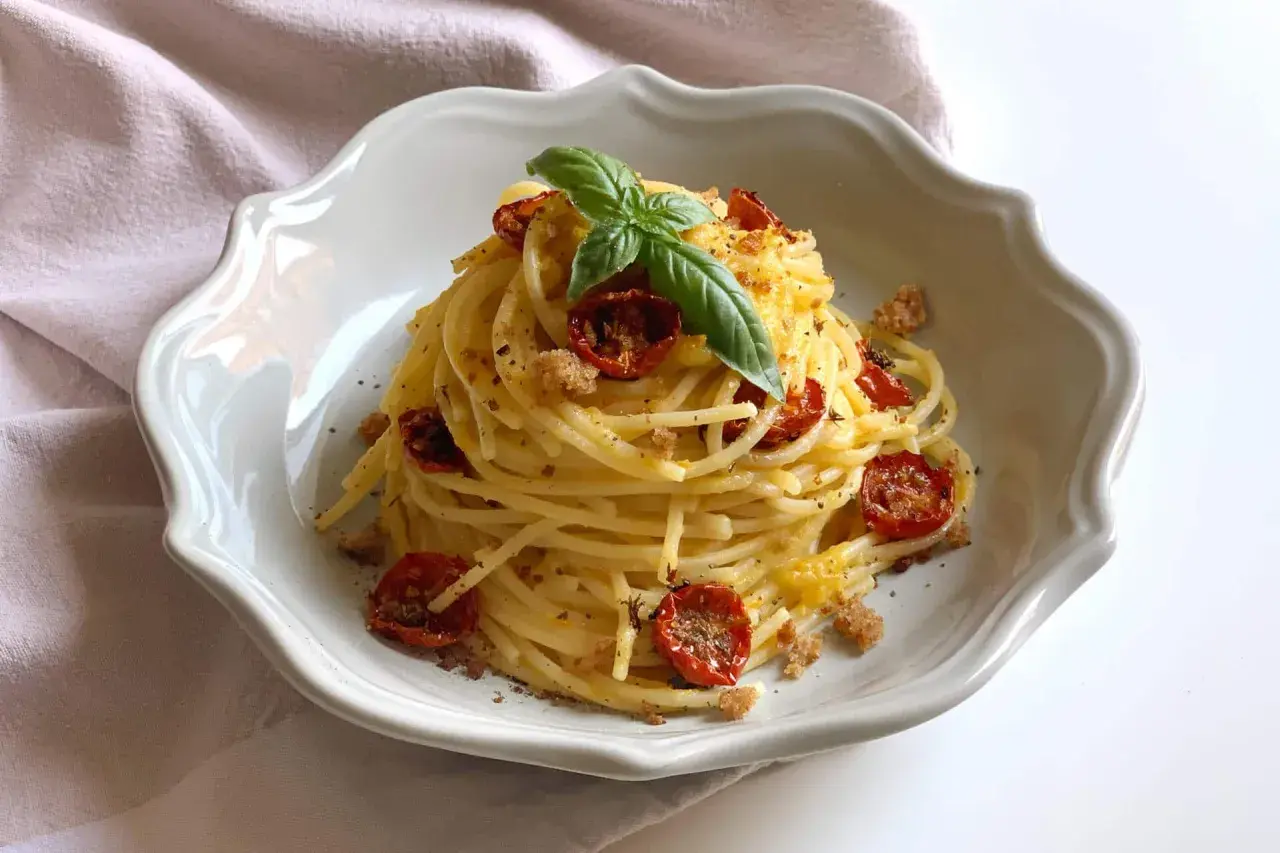 Un piatto di spaghetti conditi con pomodorini gialli secchi, basilico fresco e pangrattato croccante.