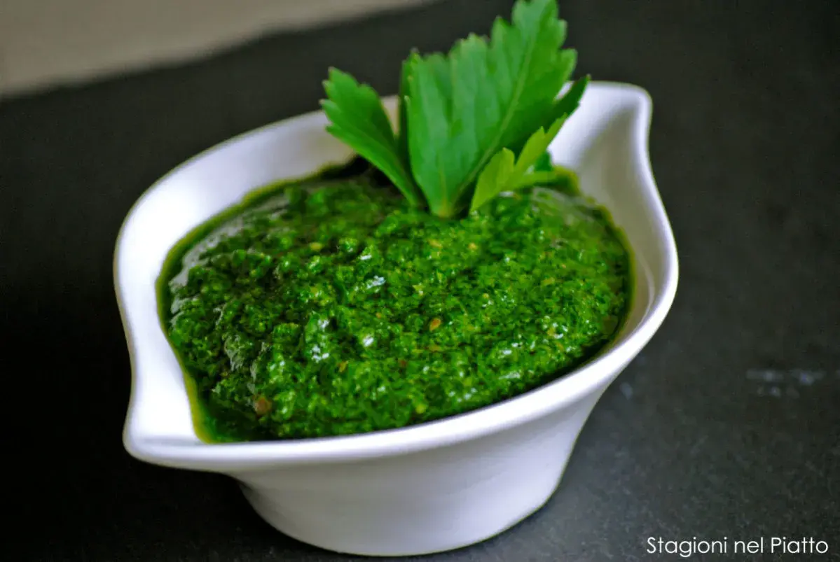 Una ciotola bianca contiene una vibrante ricetta salsa verde leggera, guarnita con prezzemolo fresco.
