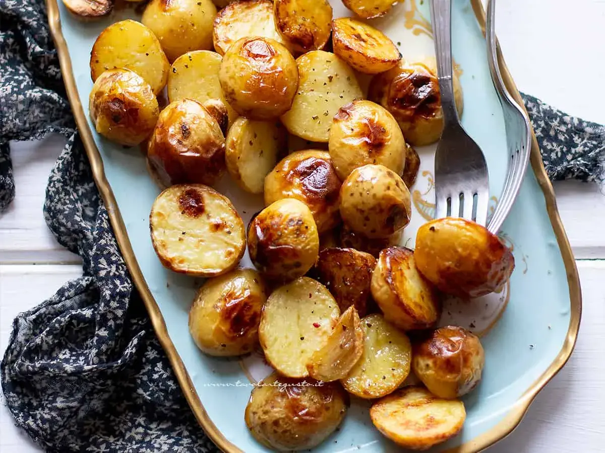 Patate novelle al forno dorate e croccanti, servite su un piatto azzurro con forchette.