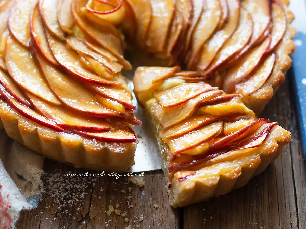 Una fetta di crostata di mele dorata, con mele caramellate disposte a rosa su una base friabile.