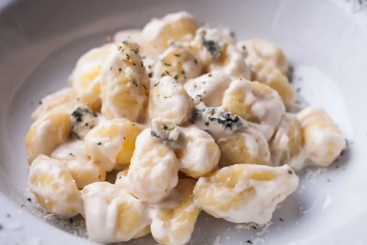 Gnocchi al gorgonzola cremosi, con pezzetti di formaggio blu e erbe aromatiche, serviti in un piatto bianco.