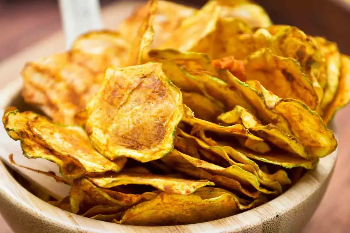 Croccanti chips di zucchine dorate, un'alternativa salutare e gustosa alle patatine, servite in una ciotola di legno.
