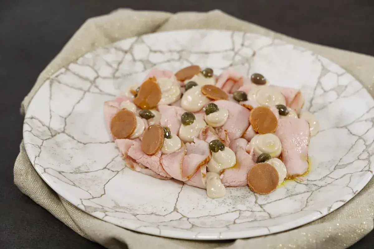 Vitello tonnato ricetta: fettine rosa di vitello, salsa tonnata, capperi e acciughe su piatto di marmo.