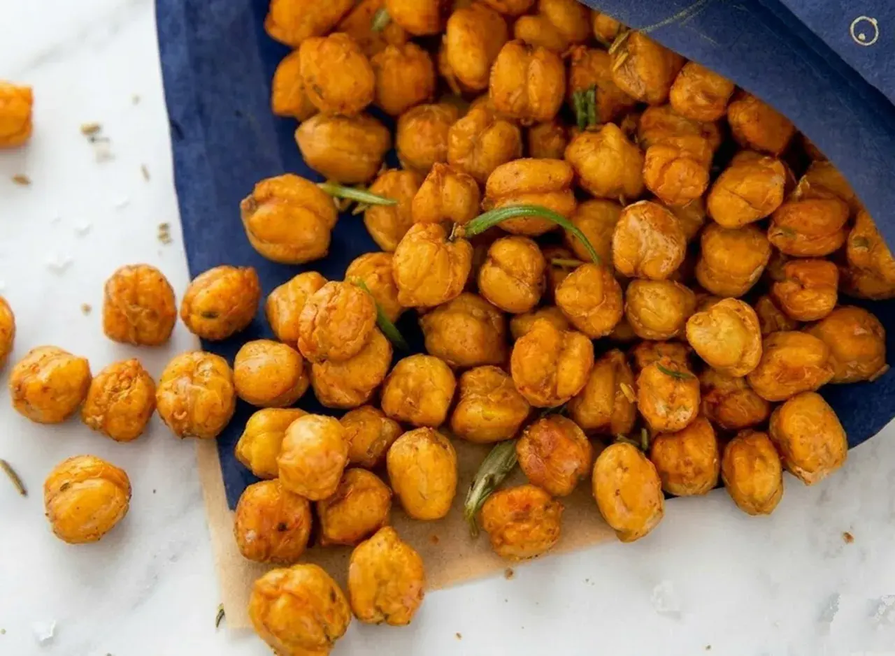 Ceci croccanti al forno, dorati e speziati, versati da un sacchetto blu. Perfetti per uno snack salutare.