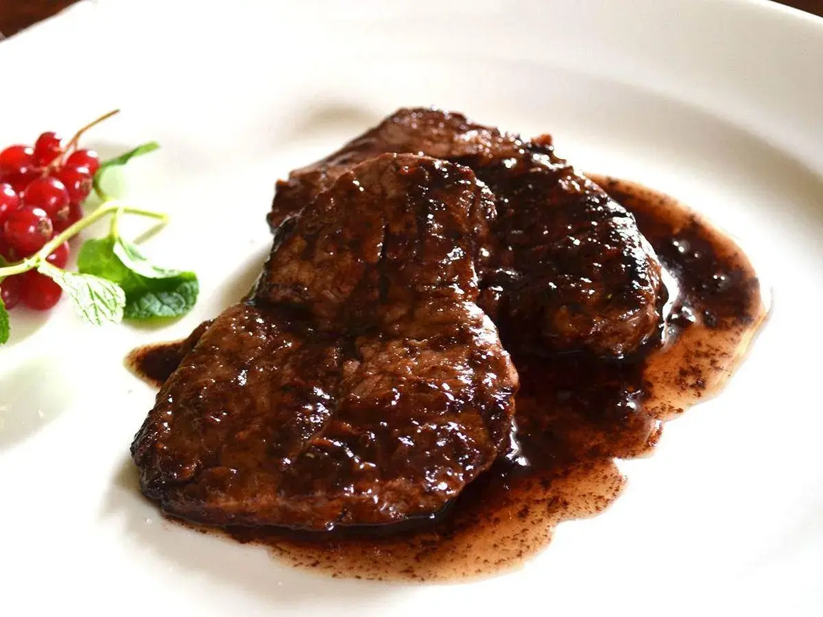 Tre fette di brasato di manzo succulento in salsa scura, guarnite con ribes rossi e menta fresca.