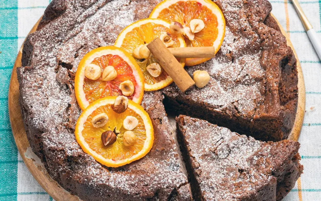 Deliziosa torta di pane al cioccolato, cosparsa di zucchero a velo, decorata con fette d'arancia, nocciole e cannella.
