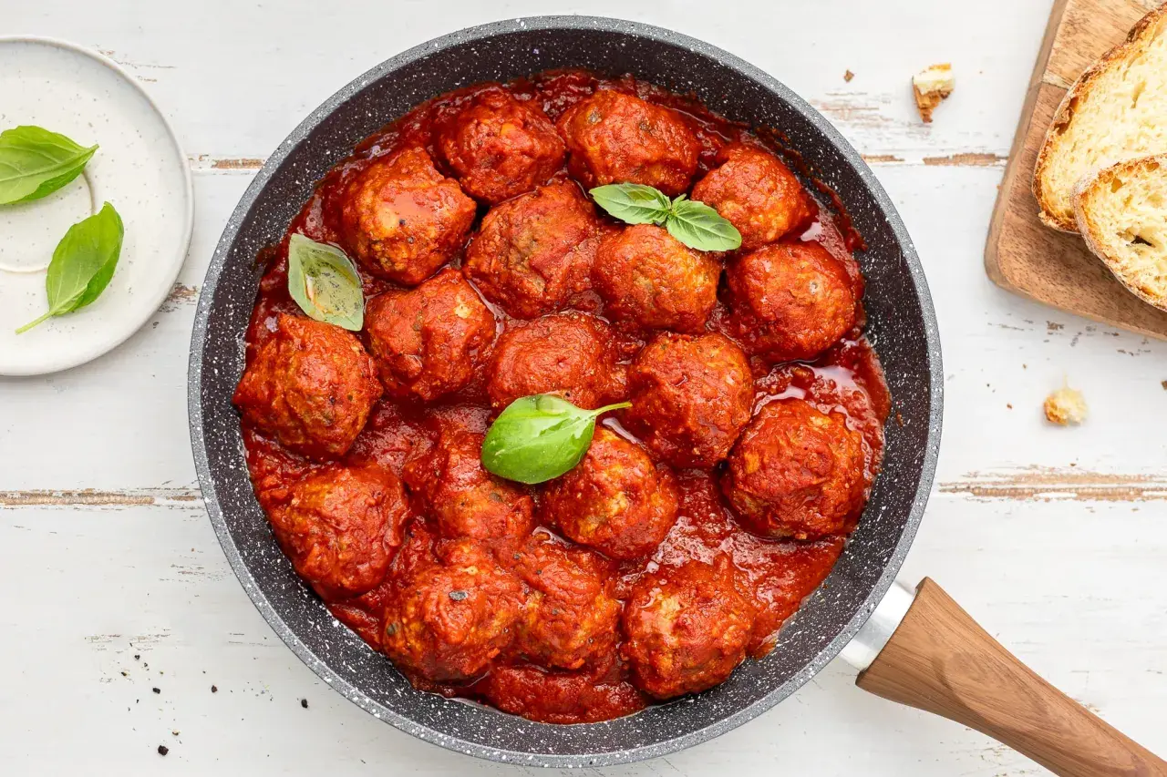 Succulente polpette di carne in padella, immerse in un ricco sugo di pomodoro, guarnite con foglie di basilico fresco.