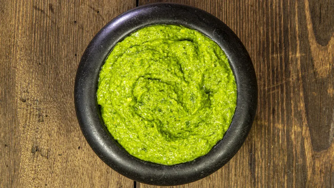 Un mortaio di pietra nera contiene un vibrante pesto alla genovese, pronto per condire la pasta.