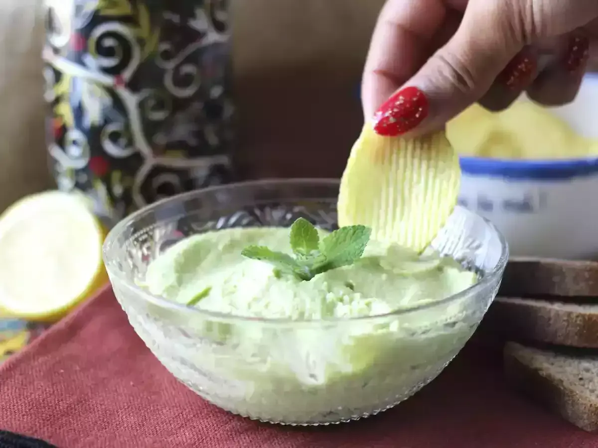 Una mano intinge una patatina in una cremosa maionese con uovo sodo, guarnita con menta.