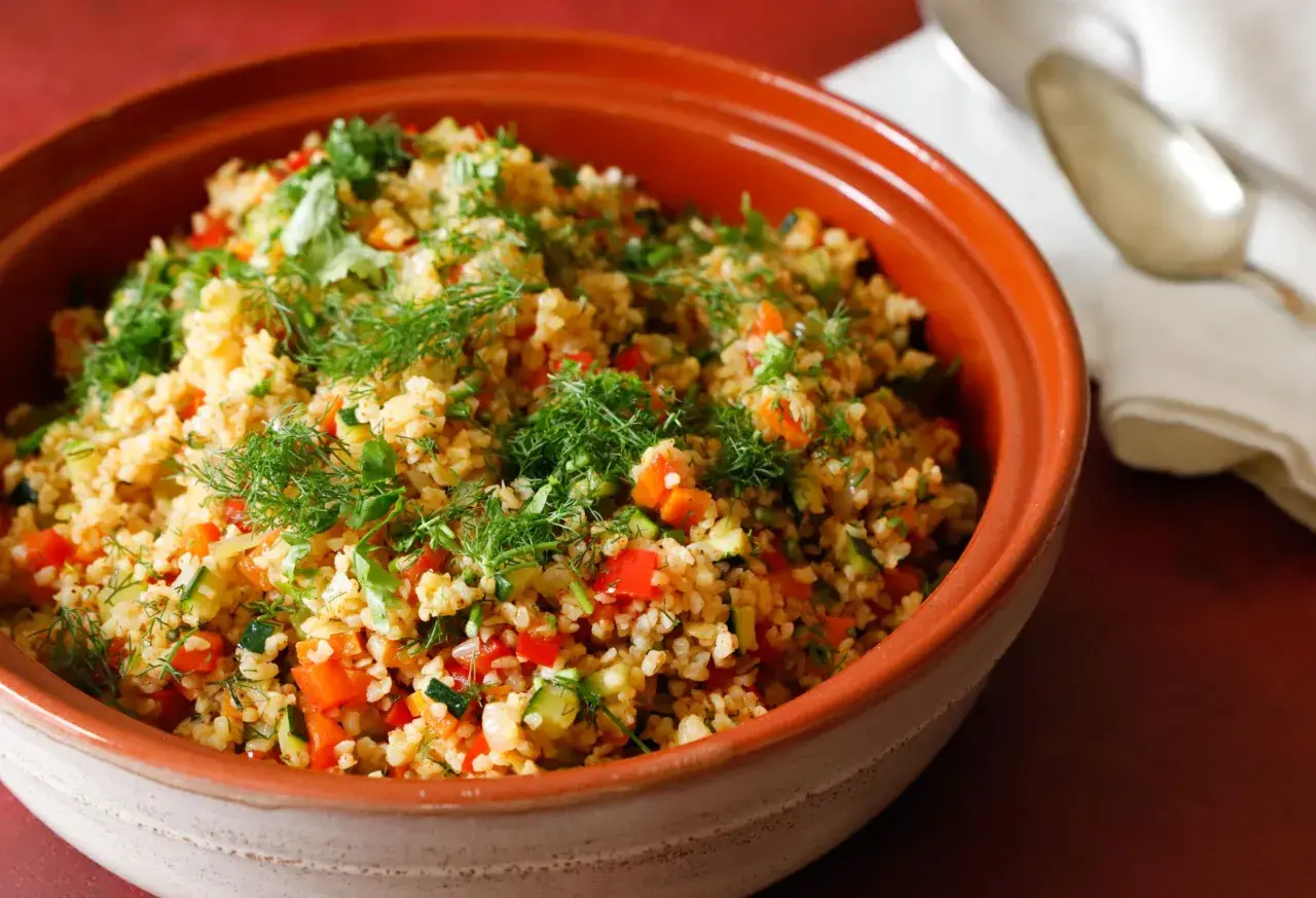 Tabulè di verdure fresco e colorato, con pomodori, zucchine e erbe aromatiche, servito in una ciotola di terracotta.